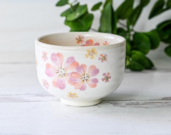 May include: A white ceramic teacup with a floral design. The cup has pink and yellow flowers on a white background.