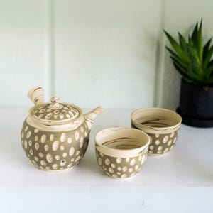 May include: A green and white ceramic teapot with a matching set of two teacups. The teapot and cups have a speckled pattern.