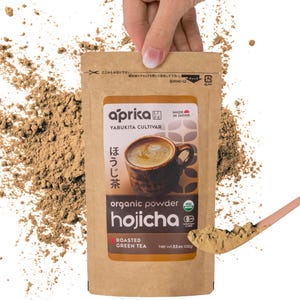 May include: A brown paper pouch with a white label that reads "aprika" and "hojicha" in black text. The pouch contains organic roasted green tea powder. The label also includes the text "Yabukita Cultivar" and "Made in Japan".