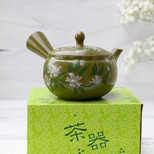 Puede incluir: Una tetera de cer&aacute;mica verde con un dise&ntilde;o floral blanco. La tetera est&aacute; sentada sobre una caja verde con un patr&oacute;n blanco y el texto "茶器" en negro.