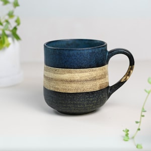 May include: A blue and brown striped ceramic mug with a wide handle. The mug has a speckled glaze and a rustic look.