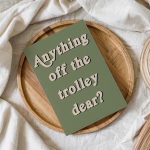 May include: A rectangular greeting card with a sage green background and the text "Anything off the trolley dear?" printed in a bold, cream-colored font with a dark shadow effect, positioned diagonally across the center of the card.
