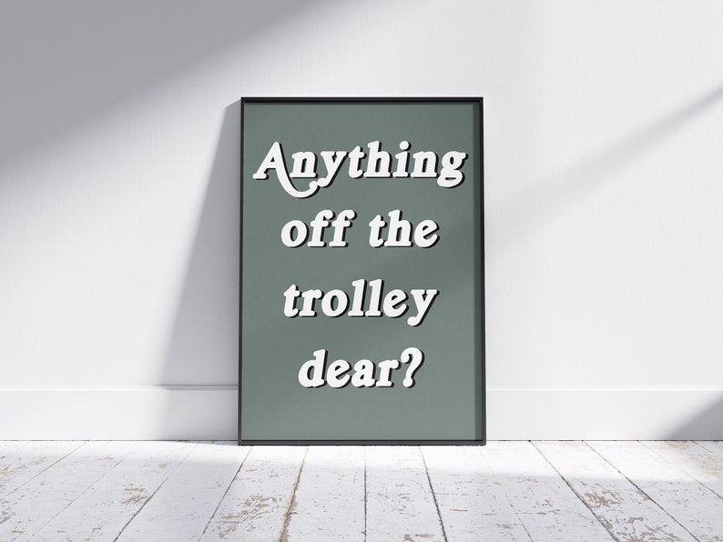 May include: A rectangular wall art print in a thin black frame featuring a muted sage green background with the white text Anything off the trolley dear? displayed in a bold, serif font. The lettering is centered and stacked in four lines.