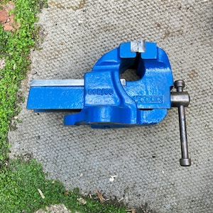 May include: A blue metal bench vise featuring a silver handle and jaw plates. The side of the tool is embossed with the text WODEN and the model number 188B/00. The vise has a sturdy cast iron body with a bright blue finish and a metallic screw mechanism.