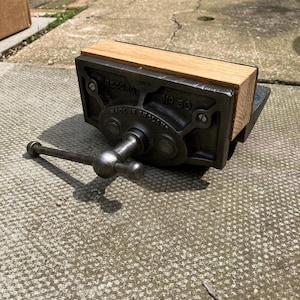 May include: A cast iron Record No 50 woodworking vise featuring a dark grey metal body with the text Record No 50 Made in England embossed on the front. The tool includes a light brown wooden jaw face and a horizontal metal handle for adjustment.