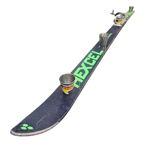 Op de afbeelding: Een zwarte ski met drie kleine metalen bekers bevestigd. De ski heeft het woord "HEXCEL" in het groen. De bekers hebben een geel en rood etiket. Skibindingen zijn zichtbaar. Een grappig item.