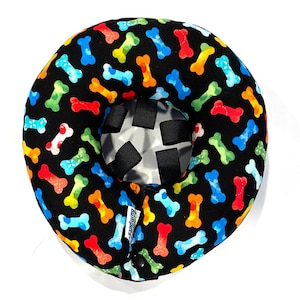May include: A black inflatable dog bone-patterned collar for pets. The collar has adjustable straps and a buckle closure. The collar is designed to help prevent pets from licking or scratching wounds.