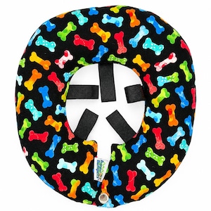 May include: A circular black pet collar bumper featuring a colorful pattern of small dog bones in red, orange, yellow, green, and blue. The accessory includes four black fabric attachment straps on the inner ring and a single metal snap closure.
