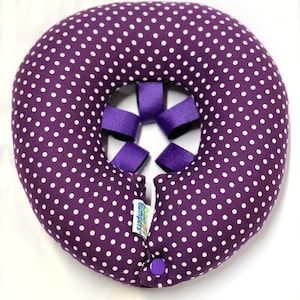 May include: Purple donut-shaped pillow with white polka dots and purple straps. The pillow has a green and blue label that says "Baby Bumpers".