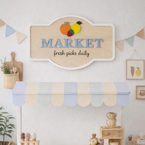 May include: A wooden market stand with a striped awning, displaying baked goods and ice cream cones. A sign above reads "MARKET fresh picks daily." The stand includes a chalkboard sign that says "Cafe open 9-4."
