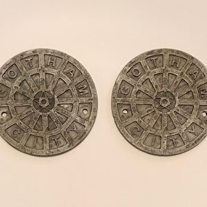 May include: Two round, gray metal manhole covers with the words "Gotham City" written around the edge.