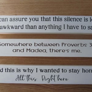 May include: Three white wooden signs with black text. The top sign reads, "I can assure you that this silence is less awkward than anything I have to say." The middle sign says, "Somewhere between Proverbs 31 and Madea, there's me." The bottom sign says, "And this is why I wanted to stay home. All this. Right here."