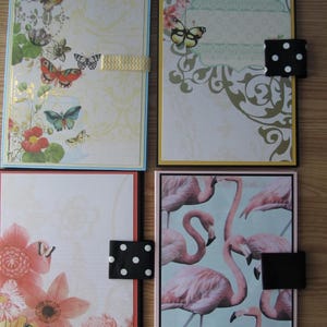 May include: Four decorative journals with patterned covers. The top left journal features butterflies and floral designs with a yellow ribbon closure. The top right journal has a butterfly and floral design with a black and white polka dot closure. The bottom journals have floral and flamingo designs.