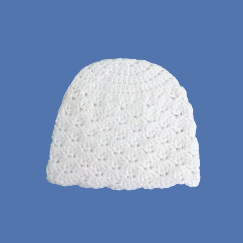 Peut inclure: Un bonnet blanc en crochet. Le chapeau est fait d'un fil doux et textur&eacute; et pr&eacute;sente un bord festonn&eacute;. Le chapeau est pr&eacute;sent&eacute; sur un fond bleu.