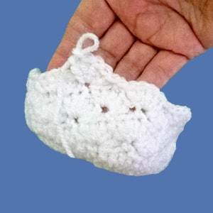 Peut inclure: Petit objet blanc crochet&eacute;, avec une boucle en haut. La pi&egrave;ce faite &agrave; la main a une surface textur&eacute;e et une forme arrondie. L'objet est tenu dans une main sur fond bleu. L'objet semble &ecirc;tre une pi&egrave;ce d&eacute;corative.