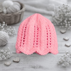 May include: A light pink, hand-crocheted hat with a scalloped brim. The hat features a textured stitch pattern with vertical openwork details. The hat is likely made of soft yarn, perfect for a baby or child.