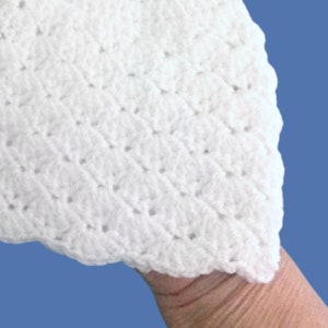 Peut inclure: Gros plan sur un article blanc crochet&eacute; avec un bord festonn&eacute;. Le motif au crochet pr&eacute;sente un design textur&eacute; en forme de losange. L'article est fait d'un fil doux et duveteux, et le fond est bleu uni.