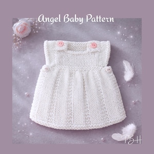 May include: A white knitted baby dress with pink buttons. The dress has a round neckline and a flared skirt. The text "Angel Baby Pattern" is at the top. The dress is displayed on a grey surface with a flower and feathers.