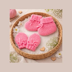 May include: A set of pink knitted baby booties and matching mittens arranged in a woven basket. The booties and mittens are made of a soft, textured yarn and feature a delicate bow detail. The basket is surrounded by white flowers and small wooden hearts.