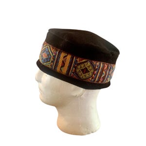 May include: A black velvet hat with a colourful patterned band around the crown. The band features geometric designs in shades of red, blue, yellow, and green.