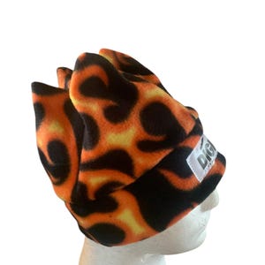 May include: A black and orange fleece beanie with a flame pattern. The beanie has a white tag with the word "DIGI" on it.