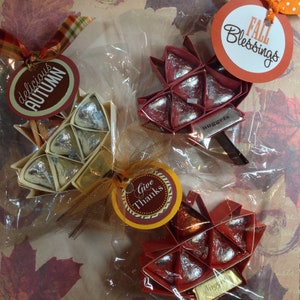 May include: Four fall-themed gift bags with red and brown paper leaves filled with chocolate candies. The bags are decorated with tags that say "delicious autumn", "give thanks", "fall blessings", and "nuggets".
