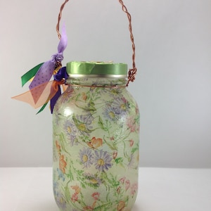 May include: A glass jar with a floral pattern and a copper wire handle. The jar is decorated with green and purple ribbons.
