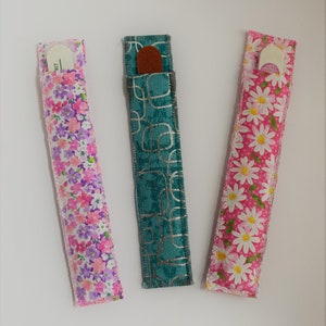 May include: Three fabric nail file holders. One is teal with a silver geometric pattern, one is pink with white daisies, and one is pink with a purple floral pattern.
