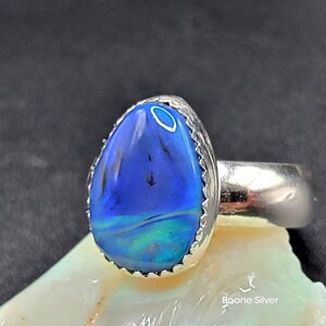 May include: A teardrop-shaped blue opal ring set in sterling silver with a decorative border. The ring is displayed on a white shell.
