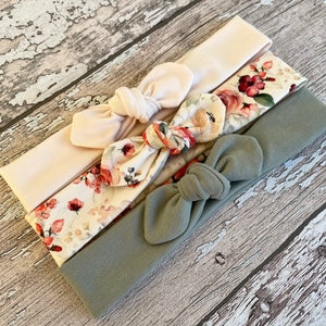 May include: Three headbands in a set. One is a solid light beige, one is a floral print with red and beige flowers, and one is a solid sage green.