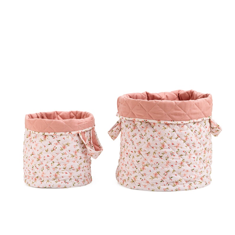 K&ouml;nnte beinhalten: Zwei rosa gesteppte Aufbewahrungsk&ouml;rbe mit Blumenmustern. Der gr&ouml;&szlig;ere Korb hat zwei Griffe und der kleinere Korb einen Griff.