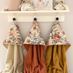 May include: Three hooded towels with floral patterns in shades of orange, yellow, and green. The towels are hanging on hooks and are made of a soft, absorbent material.