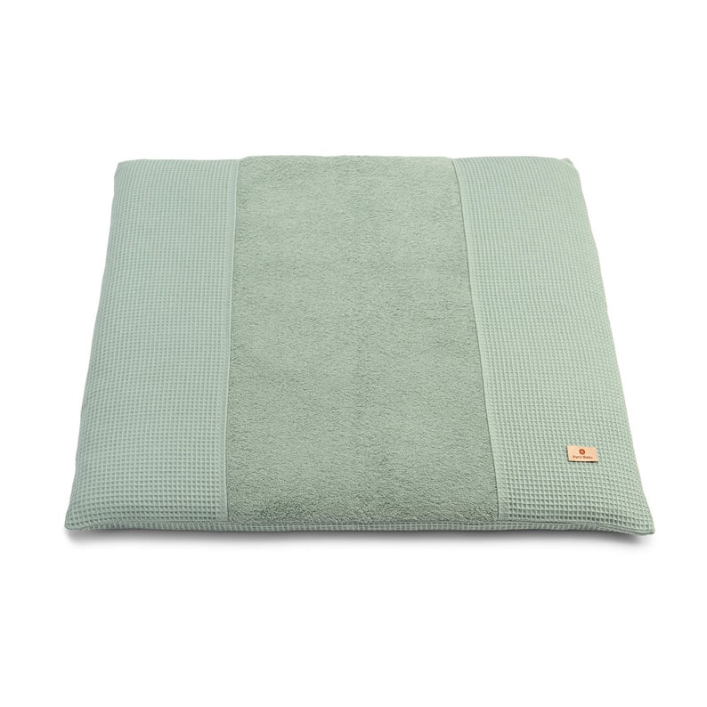 May include: A light green waffle weave changing mat with a soft, absorbent towel center. The mat has a small, rectangular label with the text "Petit Bateau" in white.