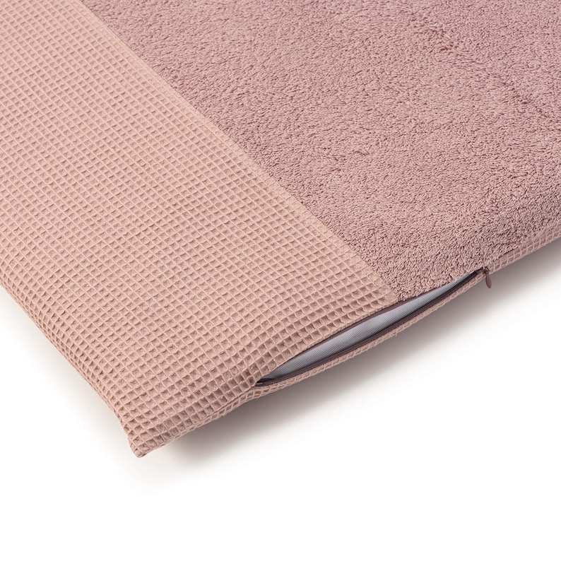 May include: A soft, blush-colored pillow with a waffle-textured side and a plush terrycloth side. The pillow has a zipper closure.