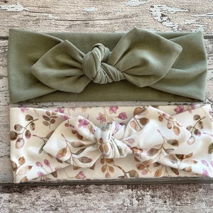 May include: Two knotted headbands, one solid sage green and one with a white background and a brown and pink floral pattern.