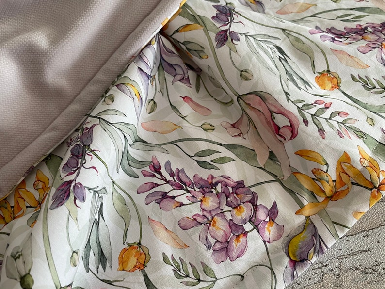 May include: White fabric with a floral print featuring purple, yellow, and pink flowers. The fabric has a subtle sheen and a soft texture.