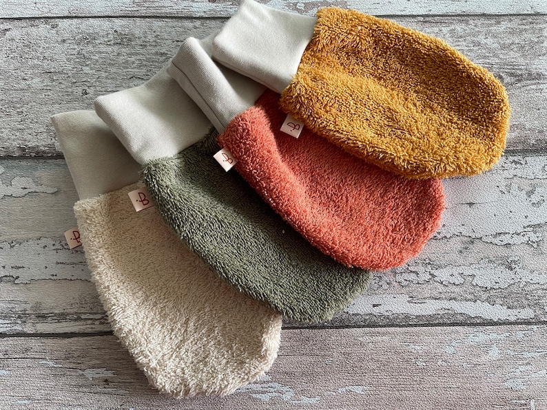 May include: Four different colored terrycloth hand mitts with white cuffs. The mitts are beige, green, orange, and yellow. Each mitt has a small white tag with a letter "B" on it.
