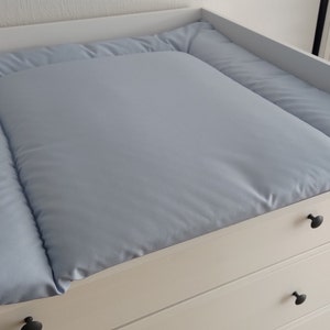 Può includere: Un fasciatoio bianco con tre cassetti e un materassino per il cambio di colore azzurro chiaro trapuntato.
