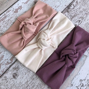 May include: Three knotted headbands in different colors: dusty rose, cream, and mauve.