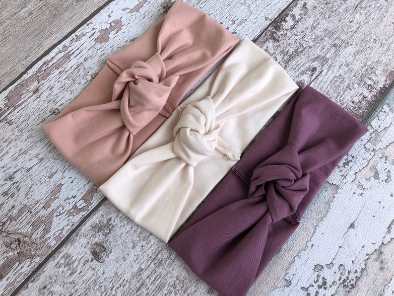 May include: Three knotted headbands in different colors: dusty rose, cream, and mauve.