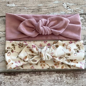 May include: Two headbands, one plain dusty rose and one with a floral pattern in shades of brown and pink on a white background.