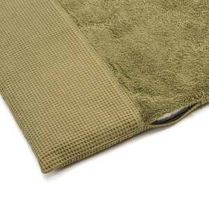 May include: A green waffle-textured fabric cushion with a soft, plush green towel fabric on the top. The cushion has a zipper closure.