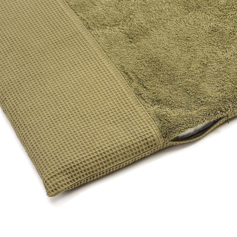 May include: A green waffle-textured fabric cushion with a soft, plush green towel fabric on the top. The cushion has a zipper closure.