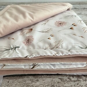 May include: A folded pink and white baby blanket with a floral pattern. The blanket is made of soft, plush fabric and is perfect for cuddling.