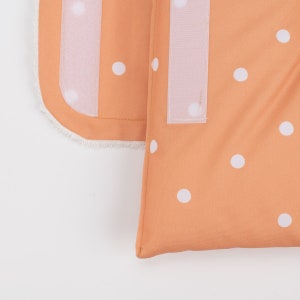 May include: A close-up of a peach-colored fabric with white polka dots. The fabric has a white velcro strip on the side.