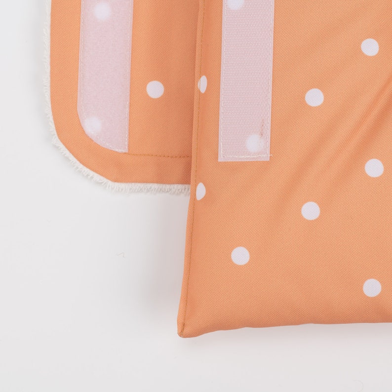 May include: A close-up of a peach-colored fabric with white polka dots. The fabric has a white velcro strip on the side.