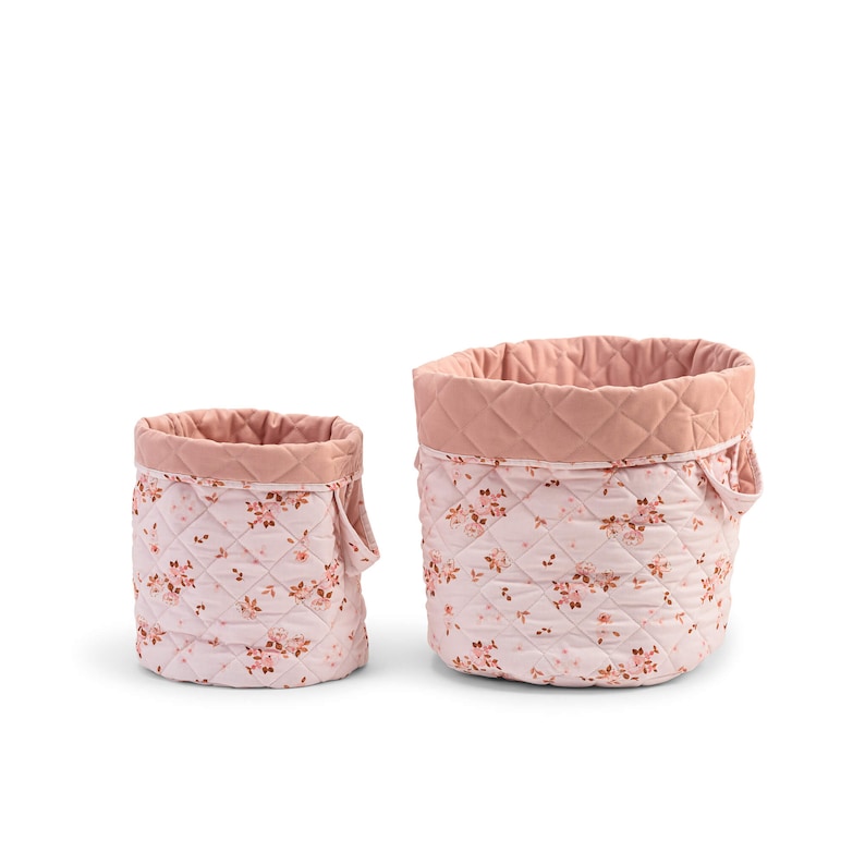 K&ouml;nnte beinhalten: Zwei rosa gesteppte Aufbewahrungsk&ouml;rbe mit Blumenmustern. Der gr&ouml;&szlig;ere Korb hat einen Griff an der Seite.