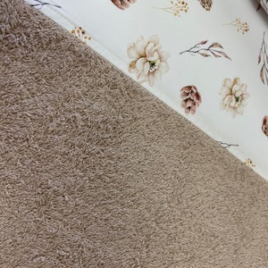 May include: A brown plush towel with a white fabric panel featuring a floral pattern with brown pine cones and branches.