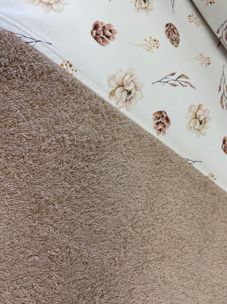 May include: A brown plush towel with a white fabric panel featuring a floral pattern with brown pine cones and branches.
