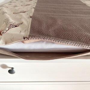 May include: A beige and brown pillow cover with a zipper closure. One side features a pattern of owls and trees on a cream background. The other side has a textured, woven appearance in a solid brown color. The pillow is resting on a white surface.